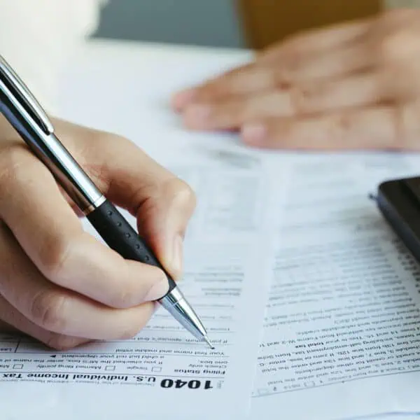 Persona revisando formularios de impuestos con calculadora y calendario marcando abril 15 de 2025, ahorrando dinero con estrategias fiscales legales.